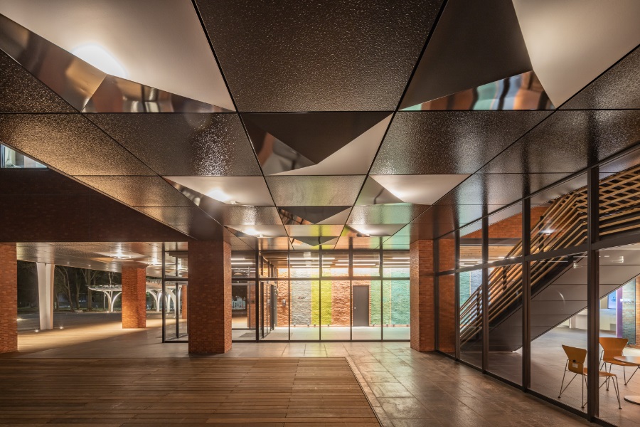 Main building porch. Repainted metal panels and newly installed recessed lighting were arranged in a checkered pattern. For the floor, we overlaid wooden floor that provided the dual advantages of eliminating the difference in surface and reducing waste. 