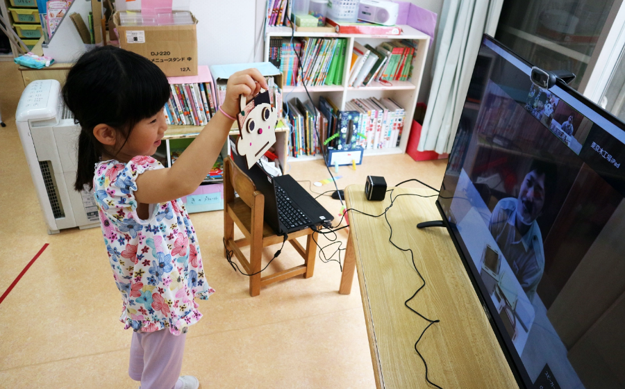 A child showing her handiwork to the teacher facing her on the screen