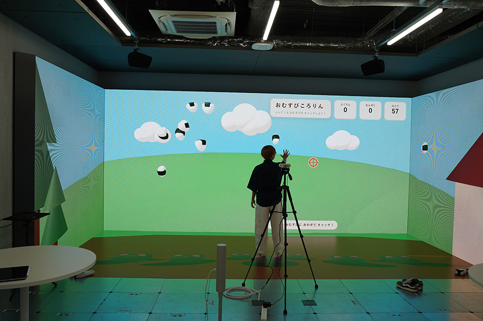 空から降ってくるおむすびをキャッチできるゲームを映し出したLEDビジョンの前に立つ濱松さん